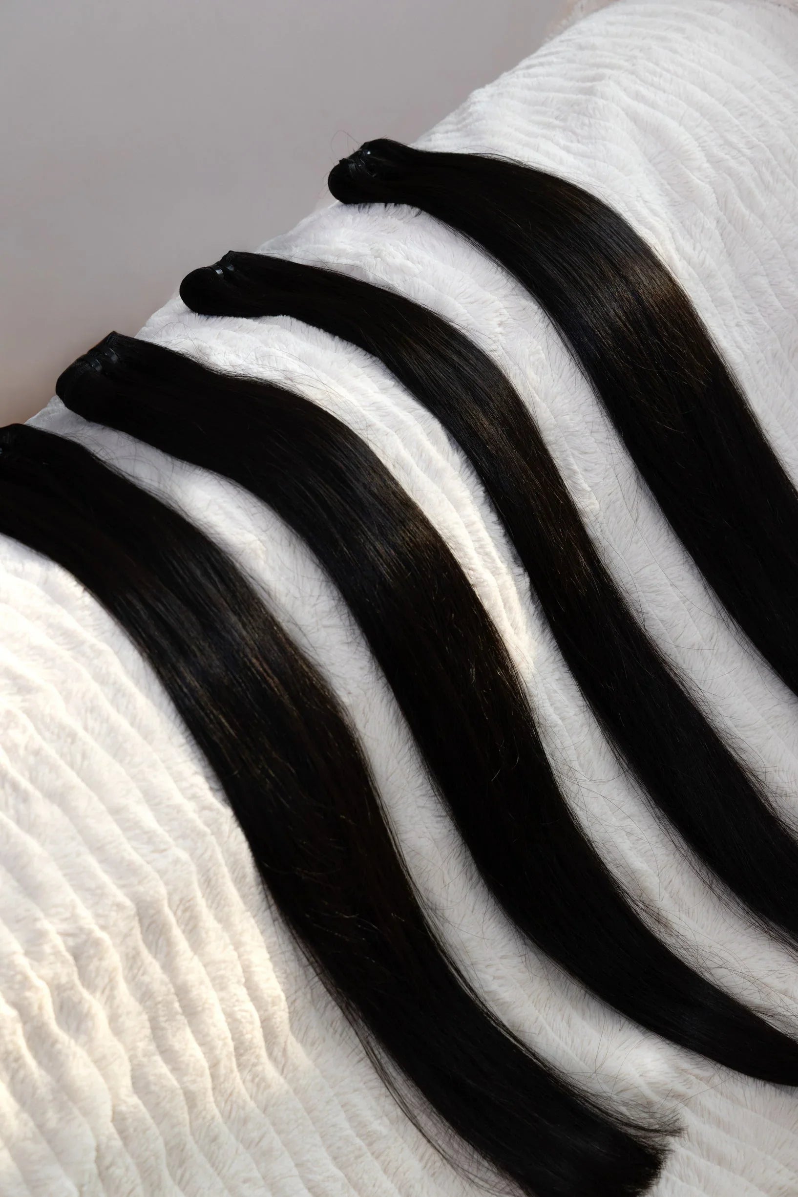 Extensions de cheveux lisses et noirs posées en rangée sur un tissu blanc texturé