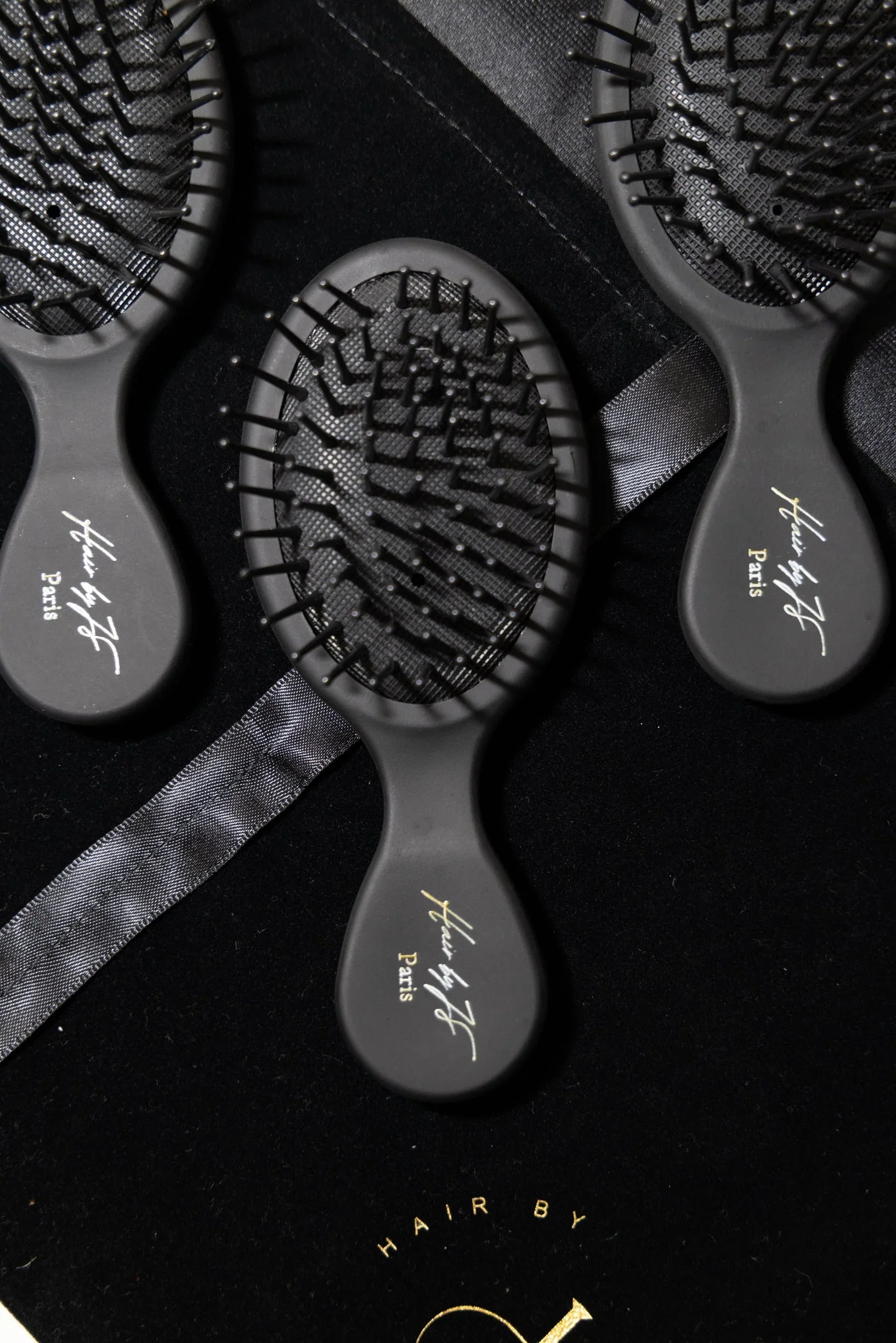 Brosses à cheveux noires avec poignée marquée Hair by JF Paris sur fond noir et ruban satin