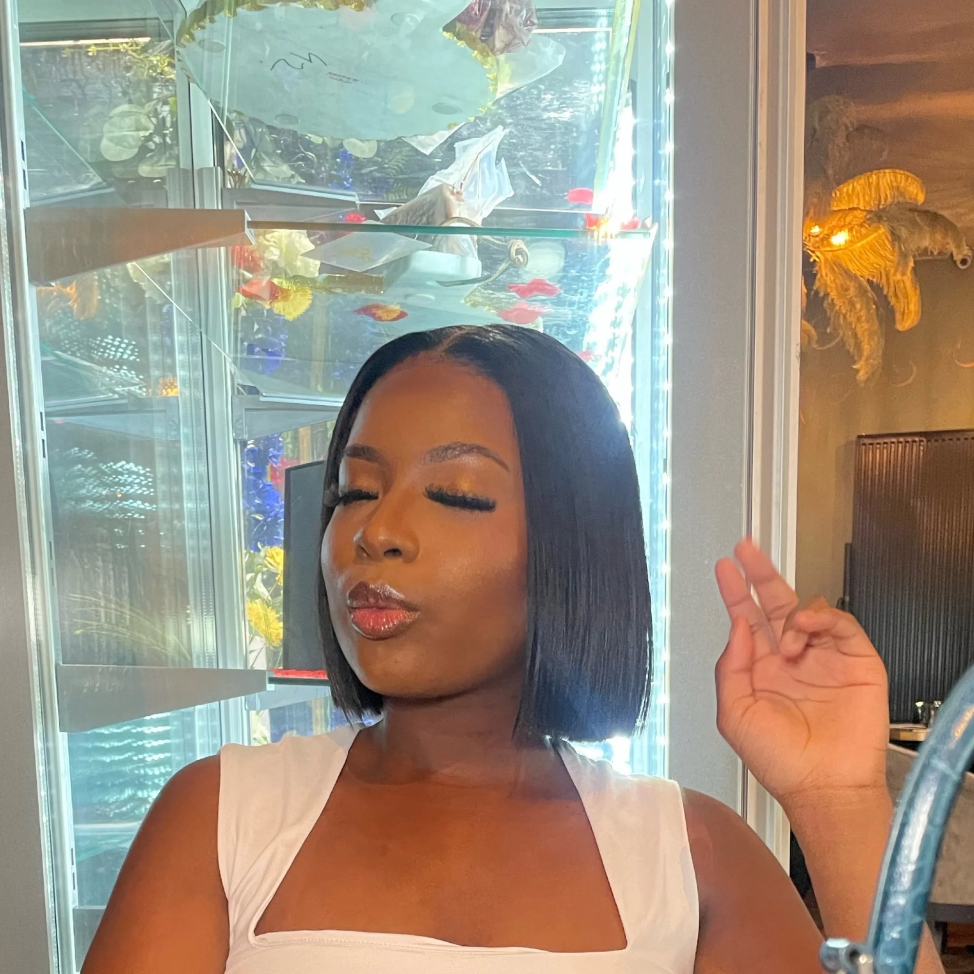 Femme afro avec maquillage brillant et coiffure carrée posant les yeux fermés dans un intérieur lumineux