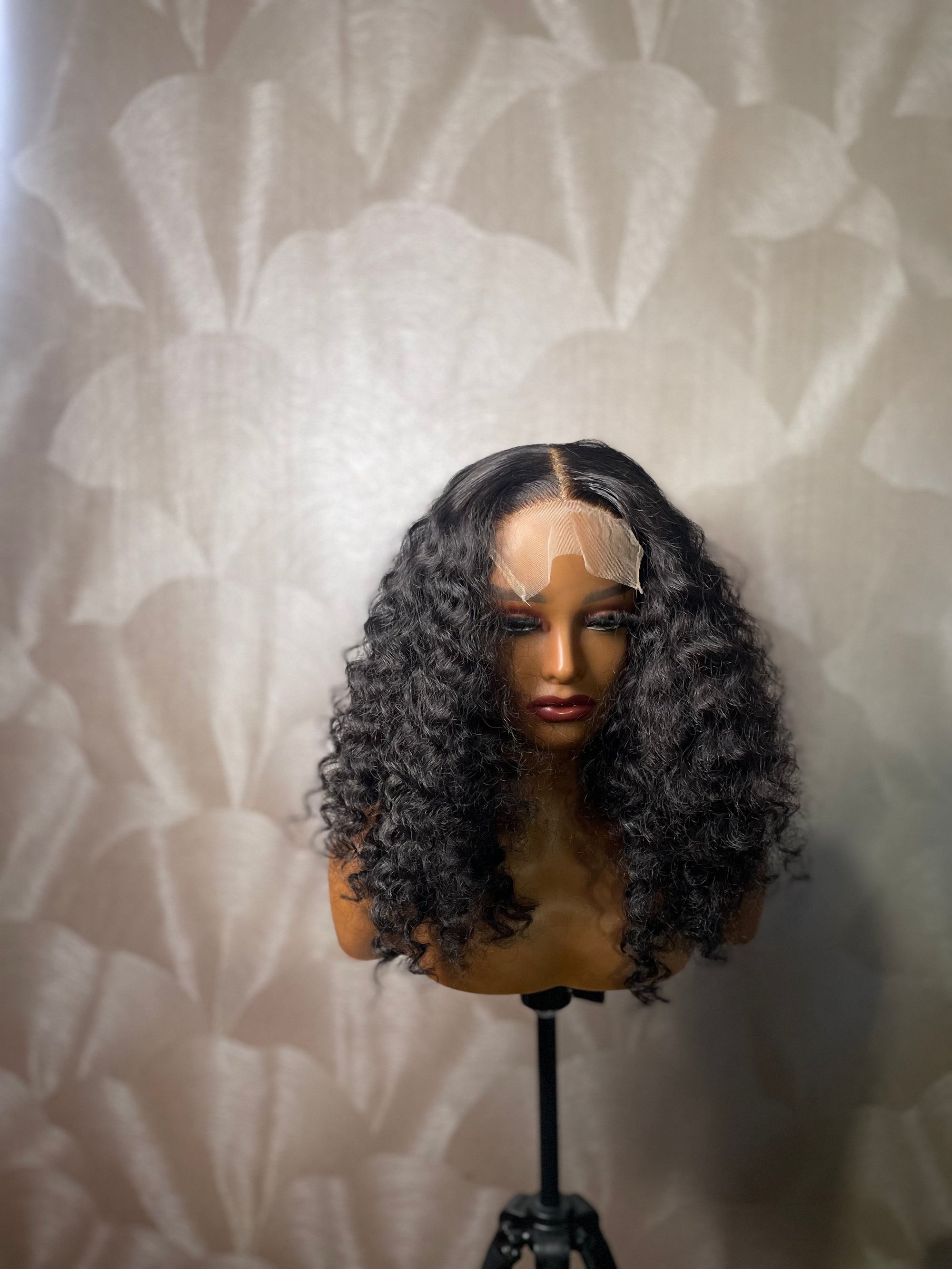 Mannequin présentant une perruque lace closure ondulée noire sur fond neutre texturé